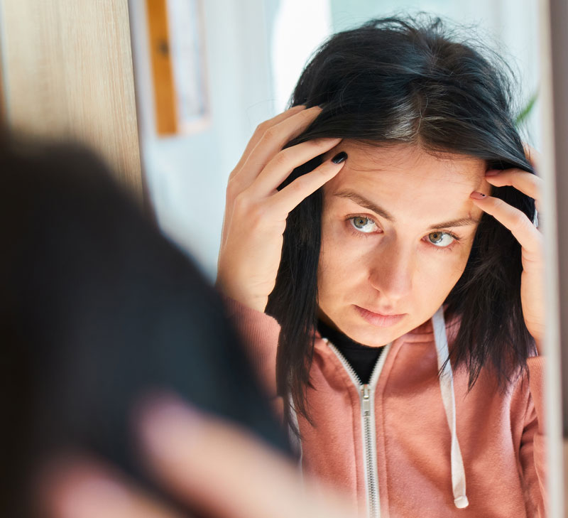Una donna controlla la stempiatura dei capelli allo specchio