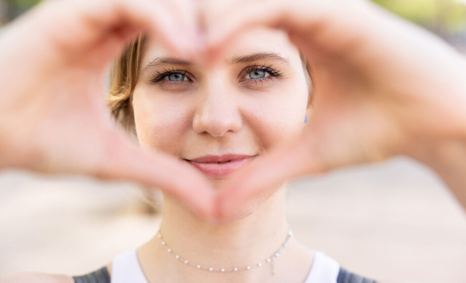 La foto rappresenta una donna che porta al volto facendo un segno di un cuore