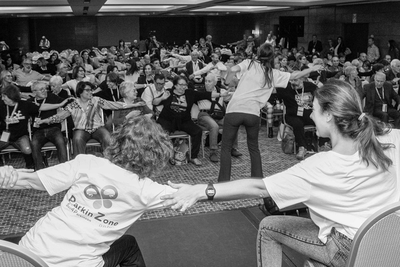 La sala del congresso Anima e Corpo dello scorso anno. La sala è piena di persone in platea che fanno esercizi guidati, dal palco, da specialisti e caregiver