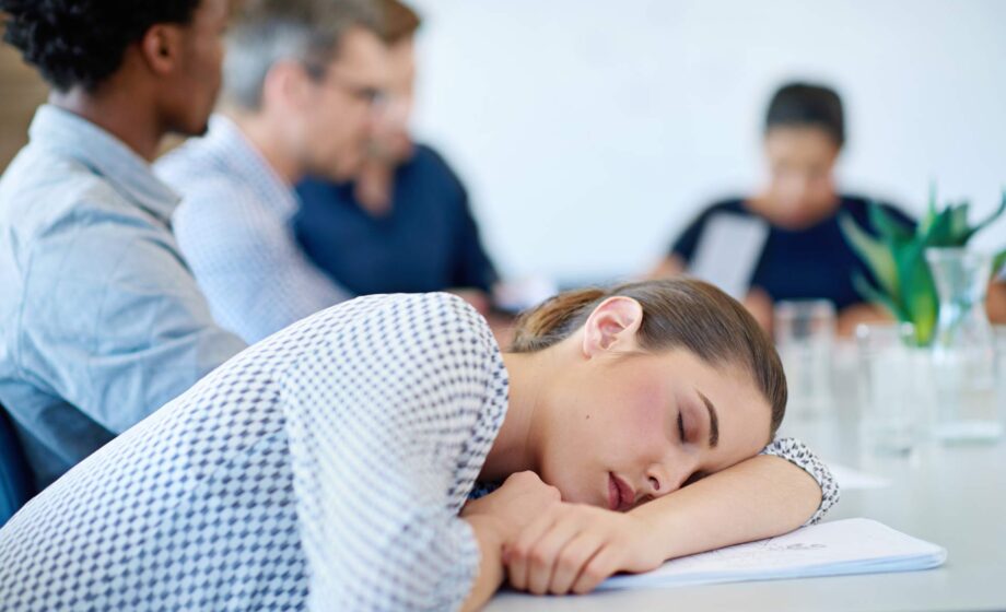 Una donna addormentata sulla scrivania durante una riunione di lavoro, affetta da problemi del sonno
