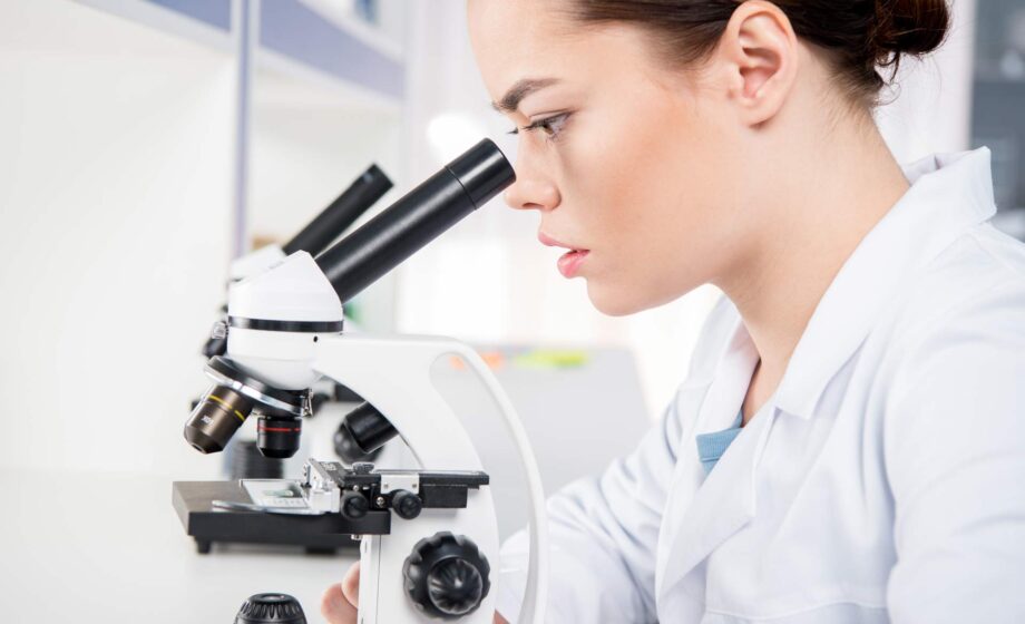 donna che sta guardando attraverso un microscopio.