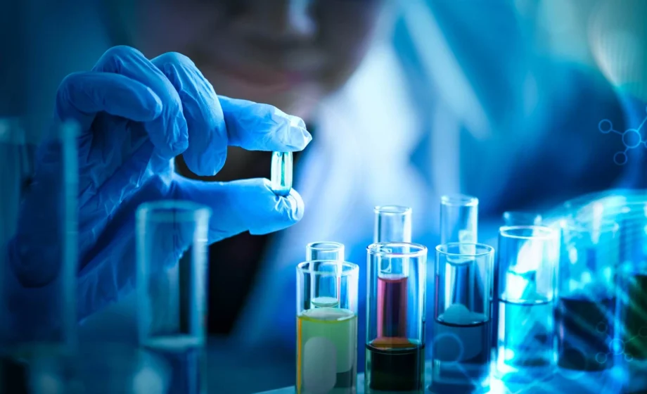 Primo piano di un ricercatore con guanti blu da laboratorio che esamina una piccola capsula trasparente.